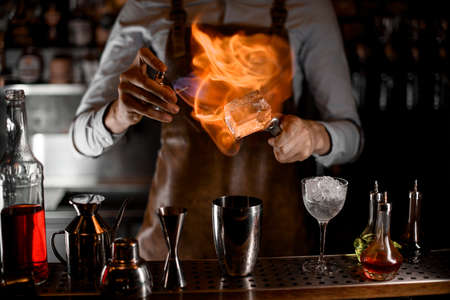 Bartender putting a fire on the big ice cube on tweezers above the steel shakerの写真素材