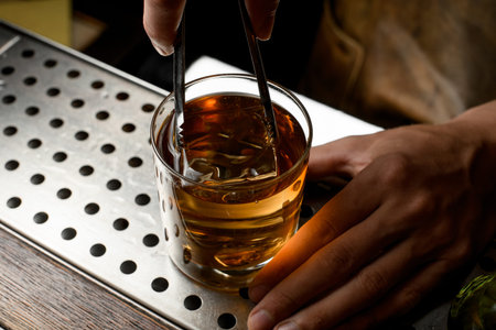 Bartender putting a big ice cube to the golden cocktail in the glass