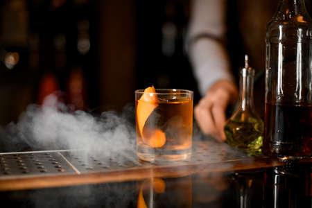 Golden cocktail in the glass with one big ice cube and orange zestの写真素材