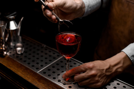Bartender putting a rose bud to the red cocktail in the glass