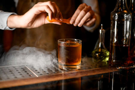 Bartender adding an orange zest juice to a golden cocktail in the glassの写真素材