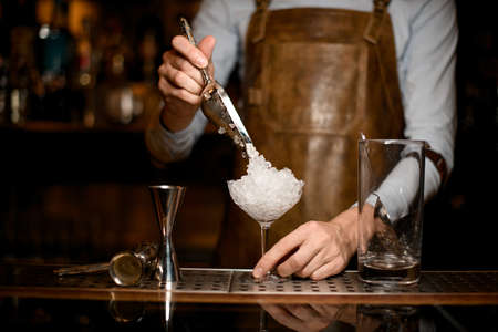 Male bartender putting crushed ice to the glassの写真素材