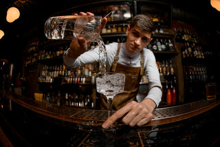 Fisheye shot attractive bartender pouring a cocktail from the measuring cup to the glassの写真素材