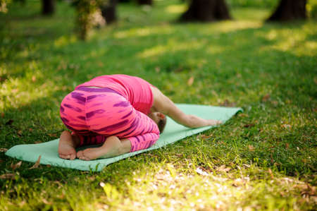 Girl in the pink sportsuit practice yoga in the park in Childs Poseの写真素材