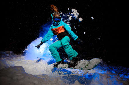 Female snowboarder dressed in a orange and blue sportswear jumping on the snowの写真素材
