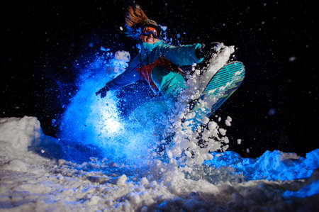 Snowboarder girl dressed in a orange and blue sportswear performs tricks on the snowの写真素材