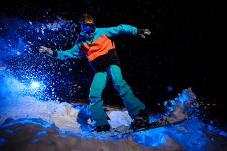 Female snowboarder dressed in a orange and blue sportswear jumping on the mountain slopeの写真素材