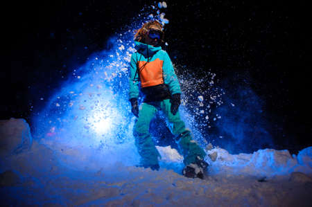 Active female snowboarder dressed in a orange and blue sportswear standing on the snowの写真素材
