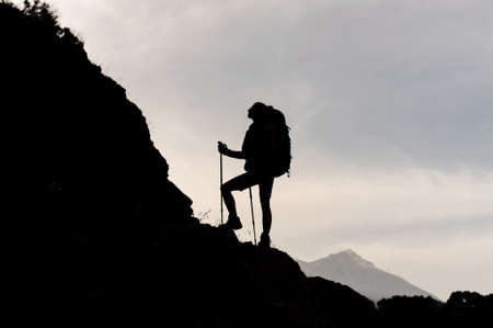 Silhouette woman standing on the rocks with hiking backpack and walking sticksの写真素材