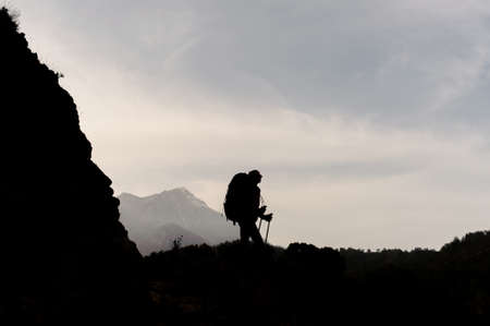 Dark silhouette woman standing on the rocks with hiking backpack and walking sticksの写真素材