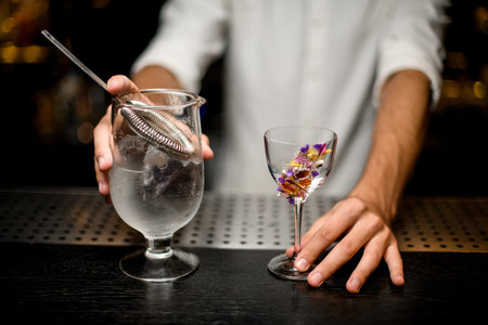 Bartender holding a cocktail measuring cup with a strainer and flower decorated glass