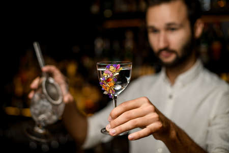 Male blurred bartender serving a cocktail in the glass decorated with flowersの写真素材