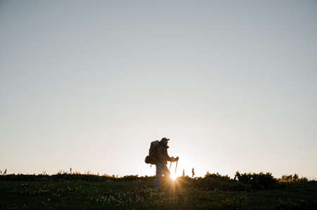 Young man standing on the hill field with hiking backpack and sticksの写真素材