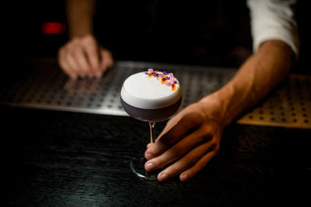 Professional bartender serving a cocktail with white scum decorated with flower petals on the bar counterの写真素材