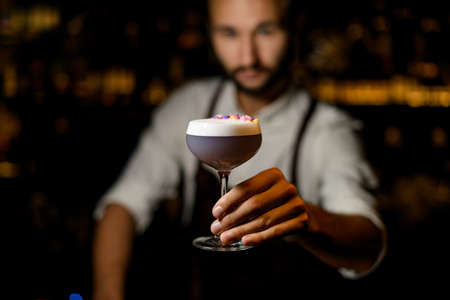 Bartender serving a cocktail with white scum decorated with flower petals in the barの写真素材