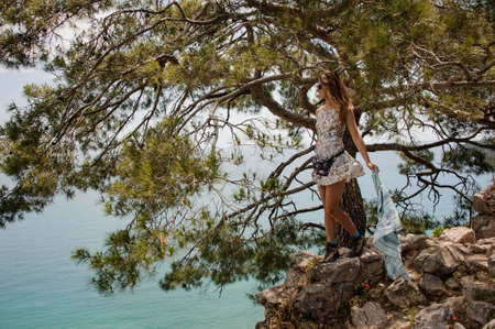 Girl in the light dress standing on the rock under the treeの写真素材