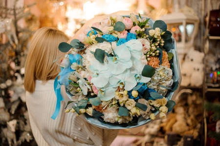 Woman holding a bouquet of pink roses silver and blue orchids in the blurred background of flower shop interiorの写真素材