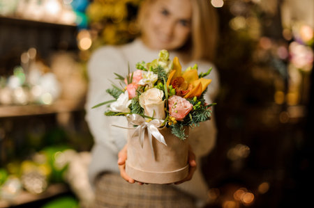 Smiling girl holding a peach color box with pink roses and yellow orchid decorated with fir-tree...