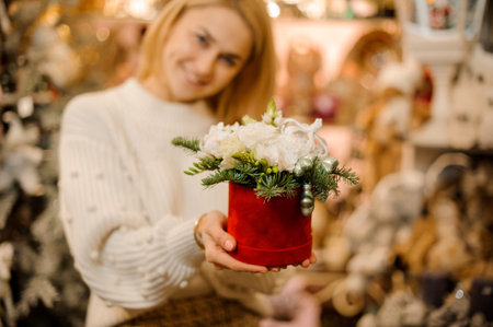 Smiling woman holding a red box with white flowers decorated with fir-tree branches