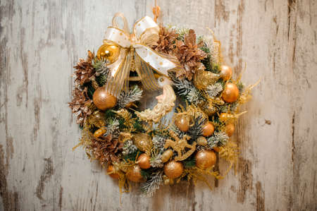 Christmas artificial wreath with golden toys, balls, tapes and glittered flowers in the background of wooden rustic wallの写真素材
