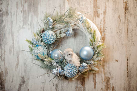 Christmas white artificial wreath with light blue decoration and little toy owl in the background of wooden rustic wallの写真素材