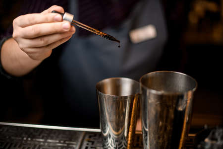 Male bartender adding a brown essence to an alcoholic drink in a steel shakerの写真素材