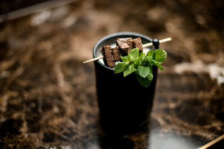 Delicious alcoholic cocktail in the black cup decorated with a brownie pieces on a skewer and mint leafの写真素材
