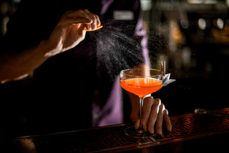 Bartender spraying on the cocktail in the glass decorated with paper airplane with clothespin with a orange zest juiceの写真素材