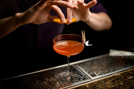 Professional bartender spraying on the cocktail decorated with paper airplane in the clothespin with...