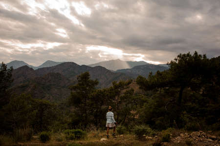 Girl with the walking sticks standing on the rock looking at the moutains through the treesの写真素材