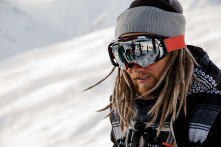 Snowboarder guy with dreadlocks standing on the slope in the protective glassesの写真素材