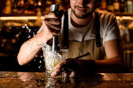 Bartender crushes lime inside cocktail glass on counterの写真素材