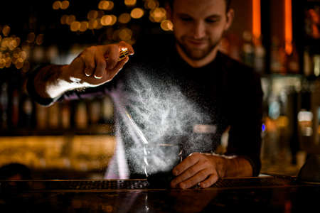 Male bartender spaying on a black glass with a delicious cocktail with essenceの写真素材