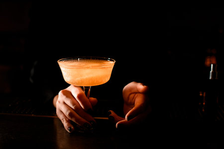 Female bartender serving transparent golden cocktail in the glass with glitter