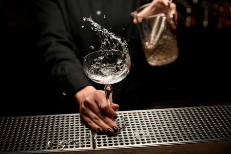 Female bartender serving cocktail in the glass with a transparent alcohol splashing itの写真素材