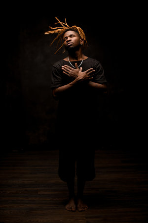 Black man with blonde dreadlocks posing in the action standing barefoot
