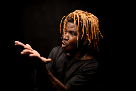 Black guy with blonde dreadlocks posing in the dark outfit with the emotional face looking at hands