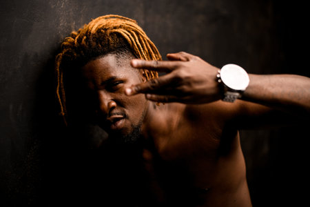 Naked black guy with blonde dreadlocks posing in the studio looking at camera showing finger gest