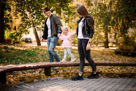 Mother and father holding their little daughter hand helping walking on the benchの写真素材
