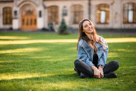 Portrait of a young woman sitting on the green grass in the autumn parkの写真素材