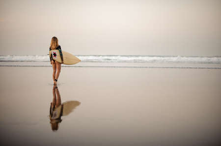 Rear view girl in the black diving suit walking on the shore to the ocean with surfing boardの写真素材