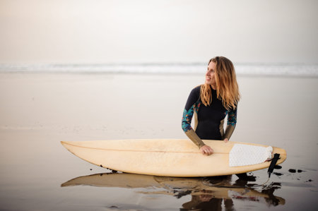 Surfer girl sitting on the sea shore with board