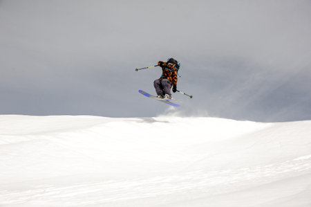 Skier jumps high in the air while sliding down the mountain during overcast weather