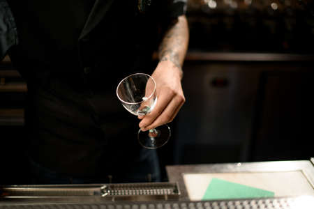 Bartender holding cocktail glass above bar counterの写真素材