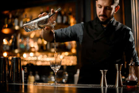 Bartender pouring vodka from glass with strainerの写真素材