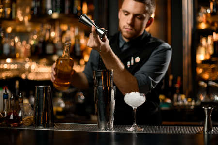 Bartender pours cognac from jigger to shakerの写真素材