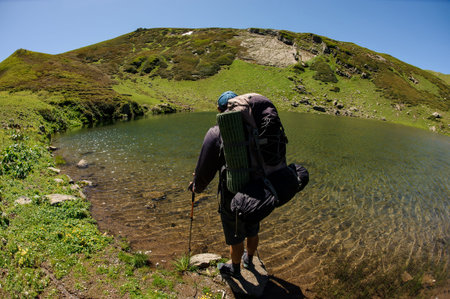 Skilled traveller with equipment stands on a big rock in small pond