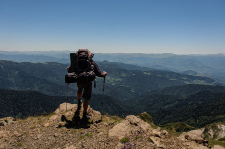 Male wanderer with equipment on mountain top looks at the scenery