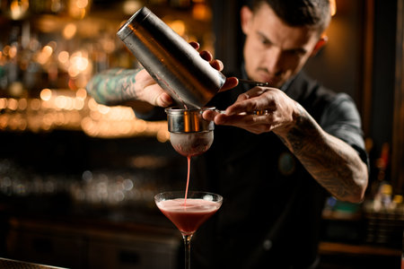 Bartender pouring cocktail from shaker through sieve