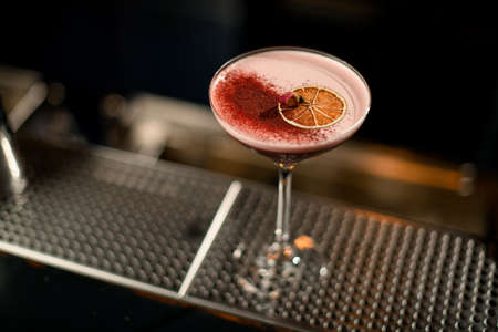 Red cocktail decorated with dried orange slice, red spices and little dried rose bud on the steel bar counterの写真素材